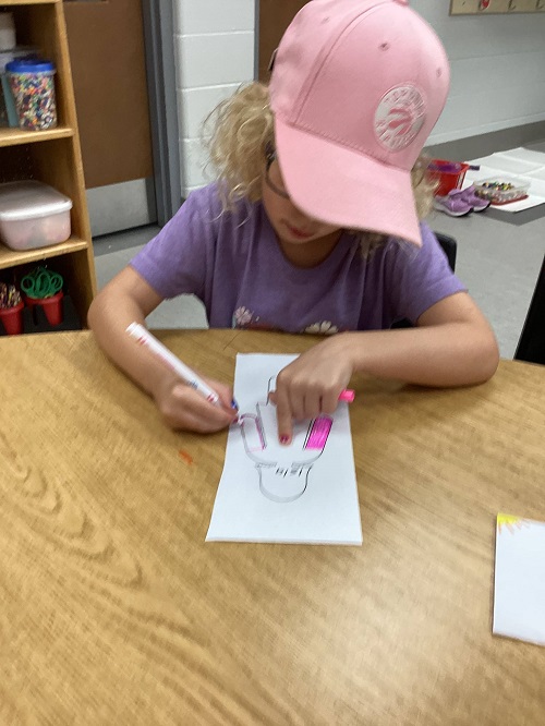 a child coloring in their cutout using a pink marker